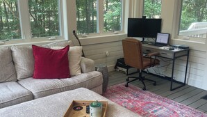 Un accogliente soggiorno con un divano grigio, un tavolino di legno con libri e bicchieri, una chitarra e una scrivania con un computer.