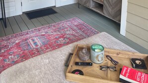 Un soggiorno con una TV a schermo piatto montata a parete, un mobiletto in legno con libri e un giradischi, un tappeto decorato e una porta con la scritta 'AMORY MISS'.