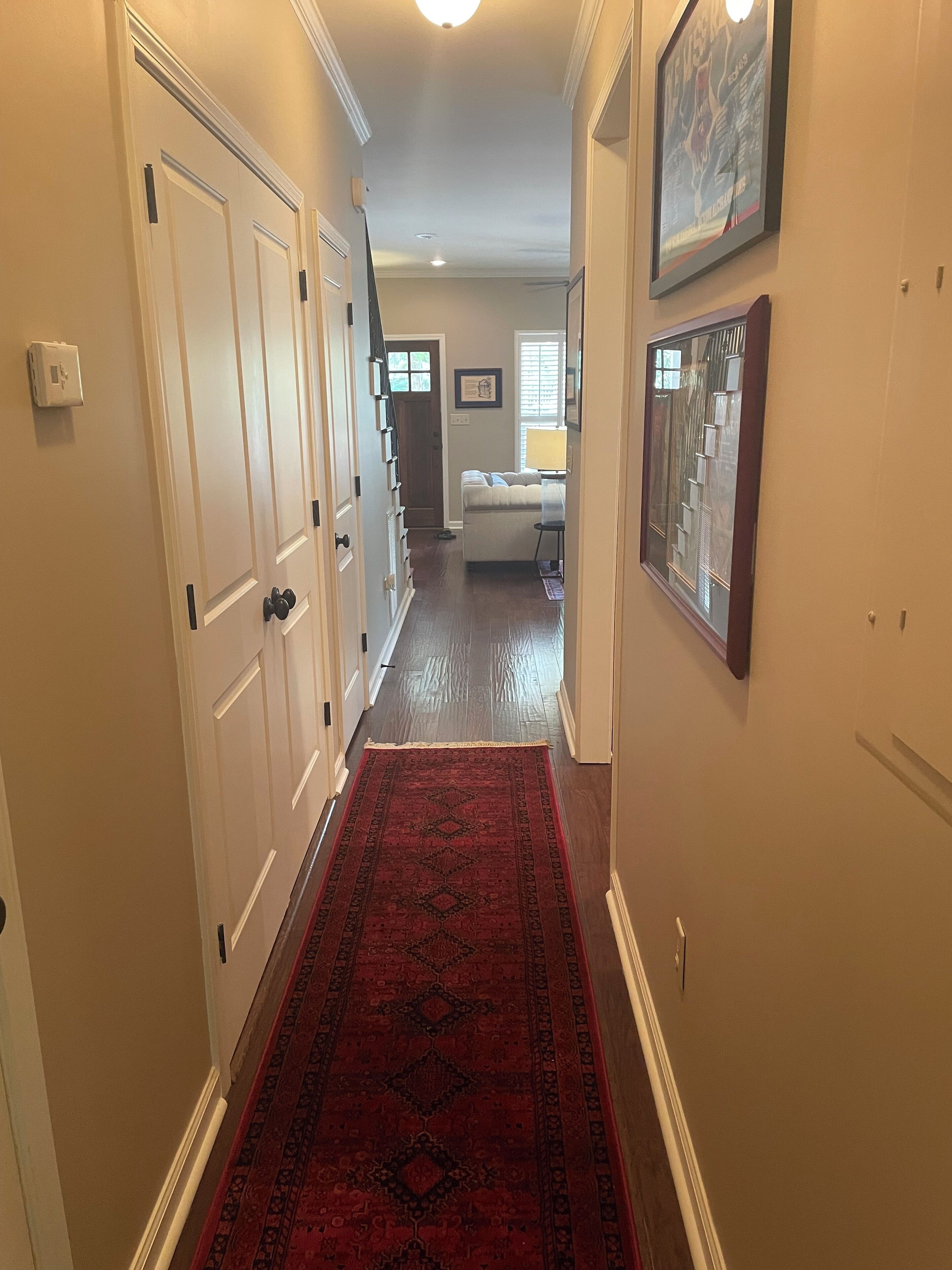 A hallway with white doors, a red patterned rug, and a framed picture on the wall.