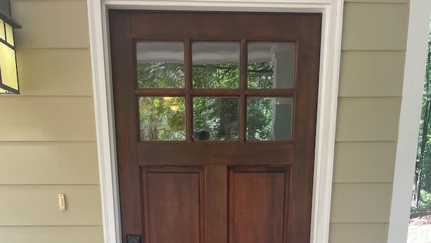 Una porta d'ingresso in legno con un vetro, un tappetino con la scritta "HOME Sweet HOME" e una ringhiera bianca sul portico.