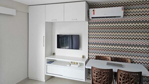 A modern living room with a flat-screen TV, white cabinetry, a dining table with chairs, and a patterned wallpaper.