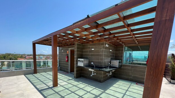 A rooftop patio with a built-in grill and seating area, surrounded by glass railings and a clear view of the cityscape.