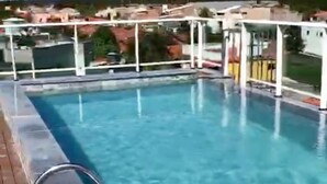 A clear swimming pool with a wooden deck and a view of a residential area in the background.
