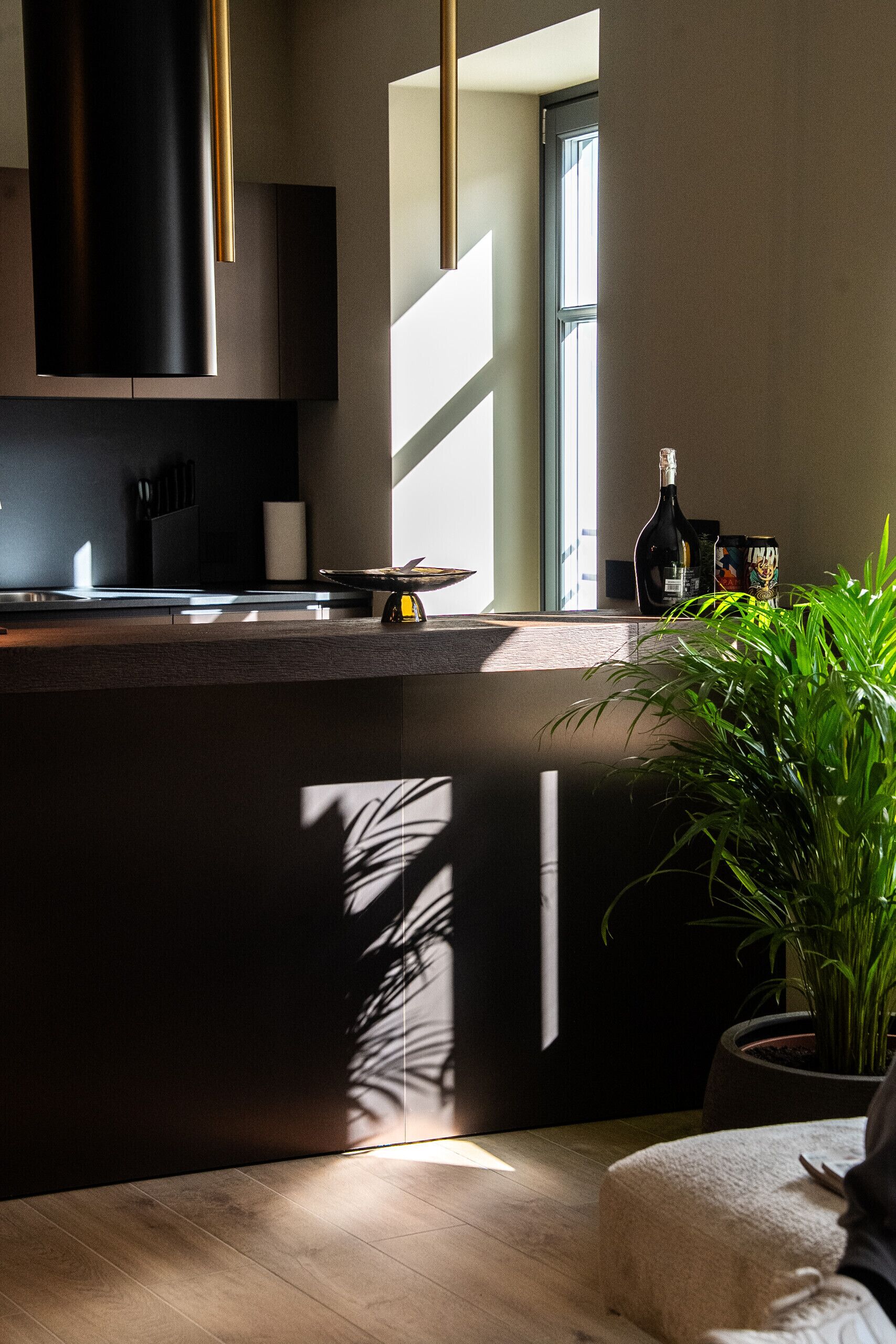 Una cocina moderna con encimera oscura, una planta en maceta y una botella de vino en el alféizar de la ventana.