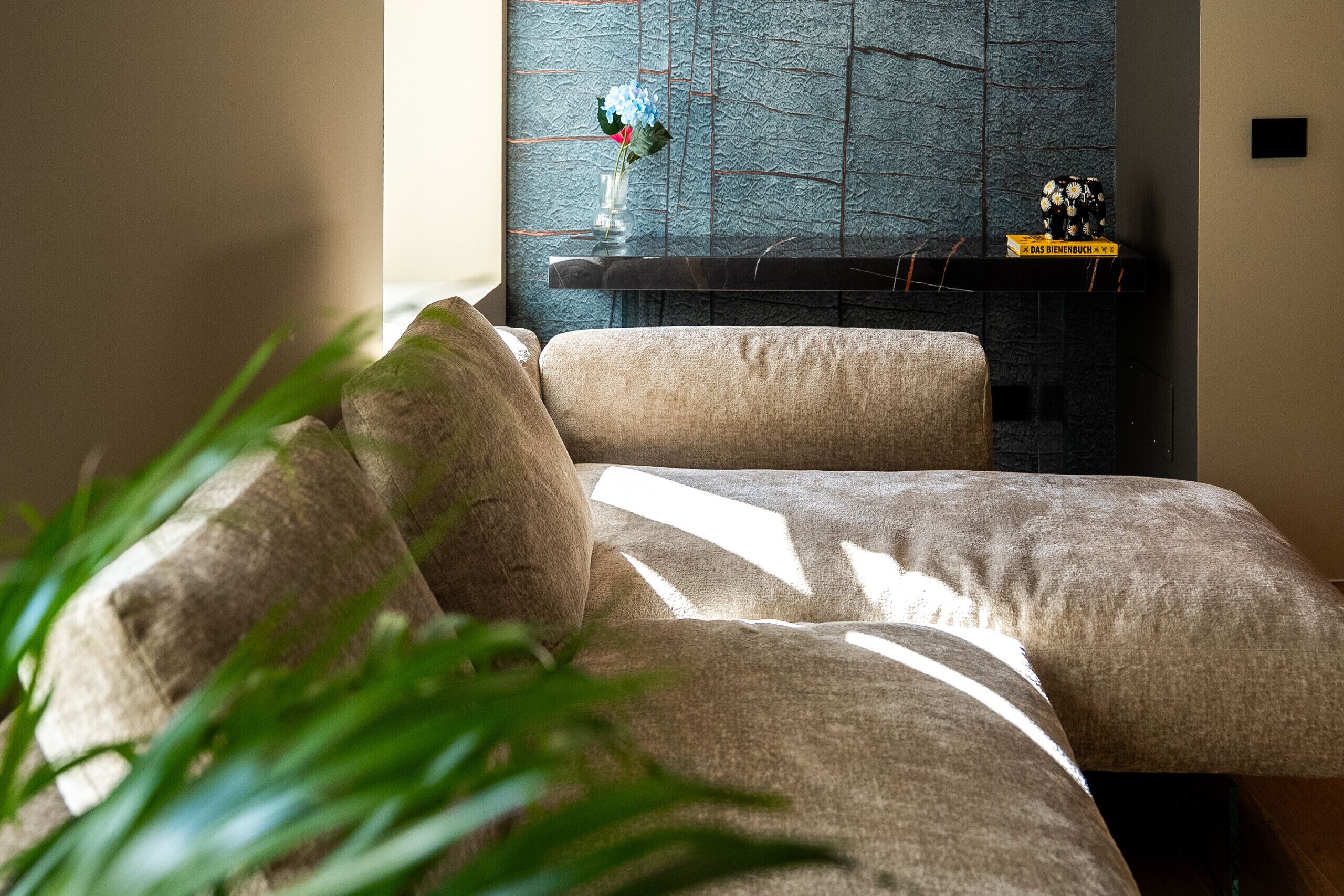 Ein modernes Wohnzimmer mit einer Couch, einer dekorativen Vase mit Blumen und einer strukturierten Wand.