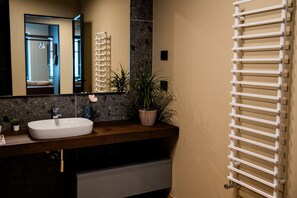 Un baño moderno con un espejo grande, un lavamanos blanco, una encimera de madera y un perchero para toallas.