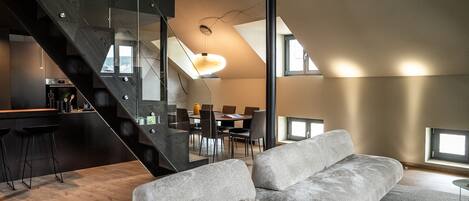 A modern interior with a staircase, a dining area, and a living room with a sofa and a coffee table.