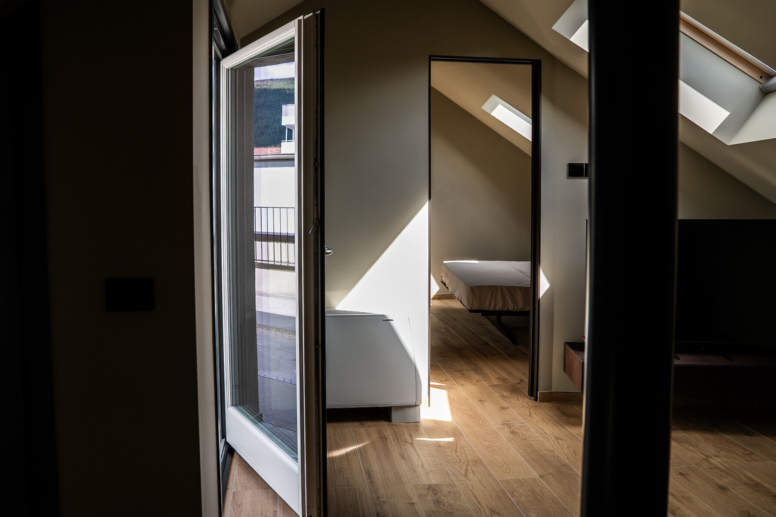 Un intérieur moderne avec un plancher en bois, un lit, une armoire blanche et une lucarne.