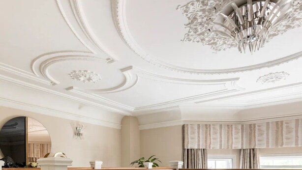 Una sala de estar moderna con un sofá redondo gris, una araña y un balcón con barandilla de cristal.