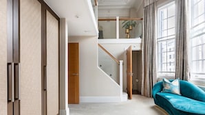 Amplia sala de estar con un sofá color turquesa, una escalera y un gran ventanal con cortinas.