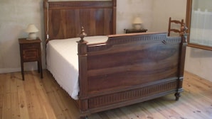 A wooden four-poster bed with a white bedspread, two bedside tables with lamps, and a mirror on the wall.