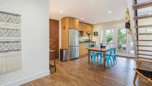 A modern kitchen with wooden cabinets, stainless steel appliances, and a dining area with blue chairs. - Charming Sag Harbor Apartment. Two blocks from Main and Bay Streets. (Sag Harbor)