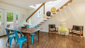 A dining area with a wooden table and blue chairs, a staircase with wooden steps, and a view through glass doors. - Charming Sag Harbor Apartment. Two blocks from Main and Bay Streets. (Sag Harbor)