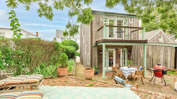 A wooden house with a patio area featuring a table and chairs, a barbecue grill, and potted plants. - Charming Sag Harbor Apartment. Two blocks from Main and Bay Streets. (Sag Harbor)