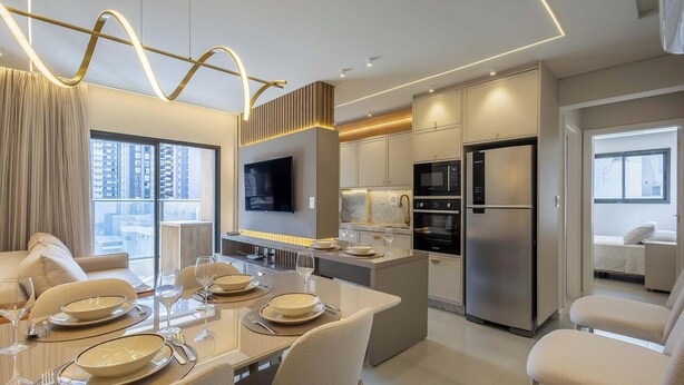 A modern kitchen with stainless steel appliances, a dining area with a glass table, and a large window offering a city view. - Apart With Barbecue 600m From the Beach Aqt0604 (Itapema)