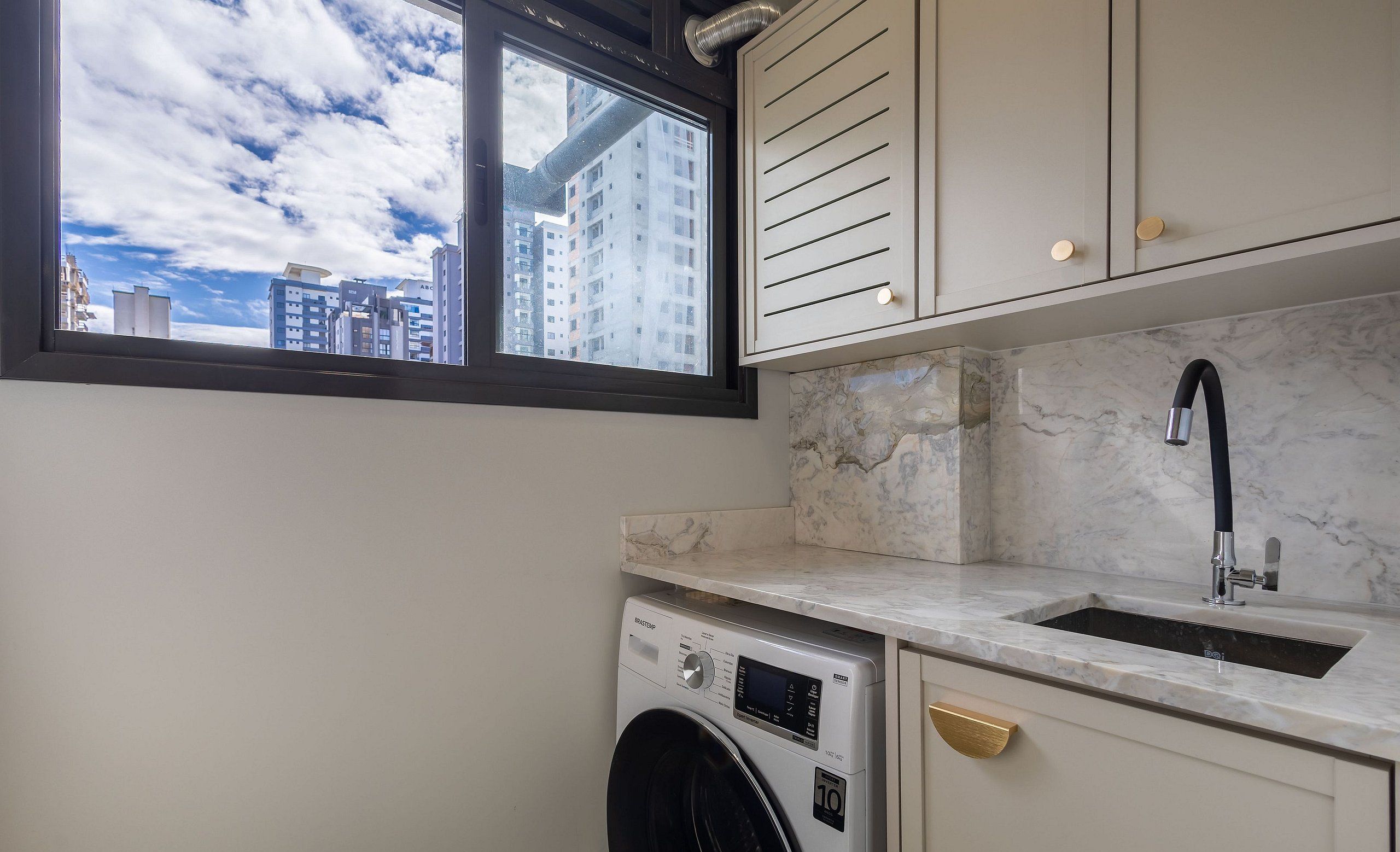 Un espace buanderie compact comprenant un lave-linge, un évier et une fenêtre donnant sur un paysage urbain.