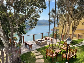 A terrace with wooden benches and tables, overlooking a lake and mountains.