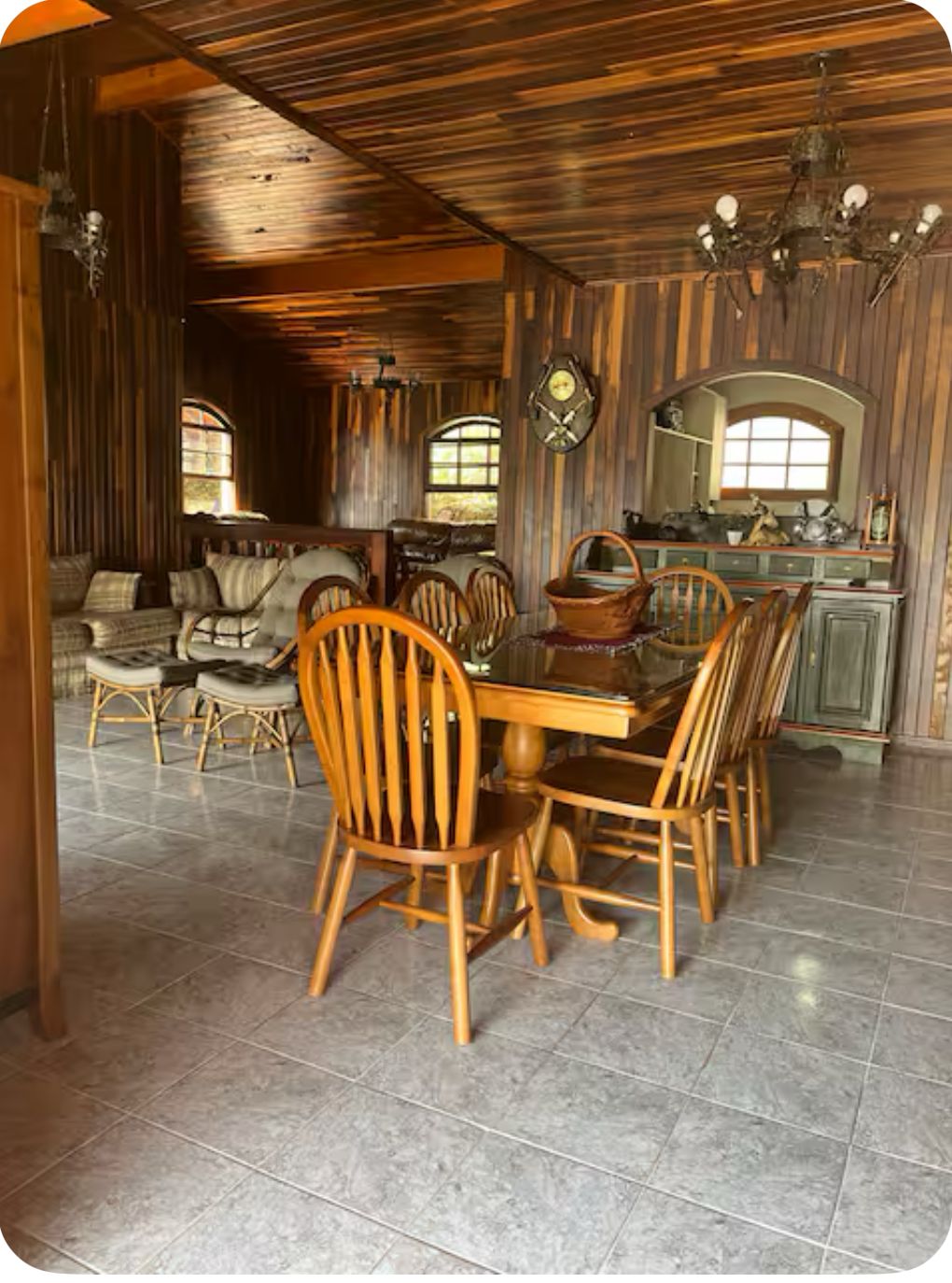 A dining area with a wooden table and chairs, a chandelier, and a kitchen in the background.