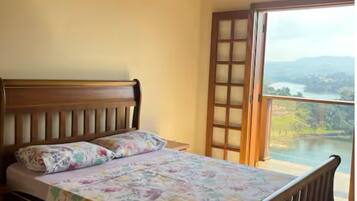 A bedroom with a wooden ceiling, a bed with floral bedding, and a view of a lake through a sliding door.