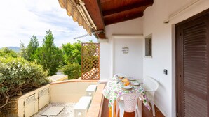 A small outdoor patio with a table set for two, a white door, and a view of greenery and trees.