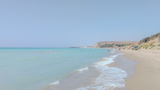 A beach with clear turquoise water, sandy shore, and a distant hill. - Villa Rosy - Your Villa Near the Sea (Marina di Butera)