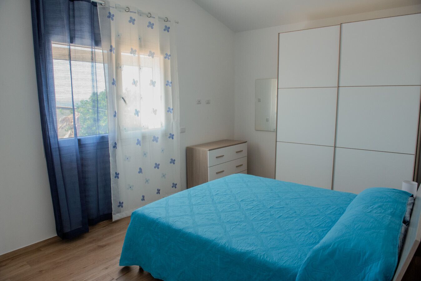A bedroom with a bed, a dresser, a wardrobe, and a window with curtains.