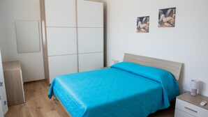 A bedroom with a bed, a wardrobe, a bedside table, and two wall-mounted paintings. - Villa Rosy - Your Villa Near the Sea (Marina di Butera)