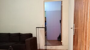 A living room with a dark-colored sofa, a wooden floor, and a door leading to another room. - Apartment in Encarnación (WRC 2025) (Encarnación)