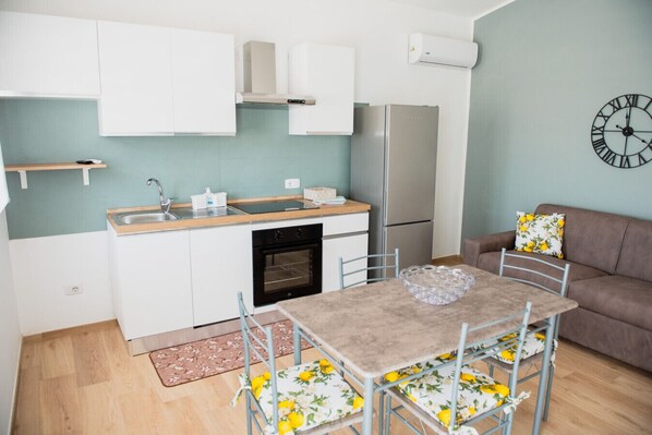 A compact kitchen with white cabinets, a stainless steel refrigerator, and a clock on the wall.