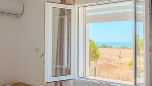 Ein Zimmer mit einem großen Fenster und Blick auf einen Strand sowie trockenes Grasland.
