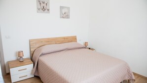 Ein Schlafzimmer mit einem hölzernen Kopfteil, einem Einzelbett mit einer gesteppten rosa Bettdecke, zwei Nachttischen mit Lampen und einem weißen Nachttisch mit Schubladen.