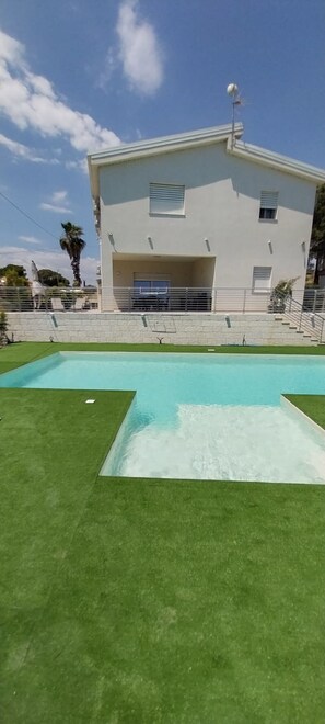 A modern building with a swimming pool, a covered area, and a clear sky.