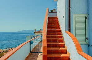A staircase leading to a balcony overlooking the sea, with a clear view of the ocean and distant hills.