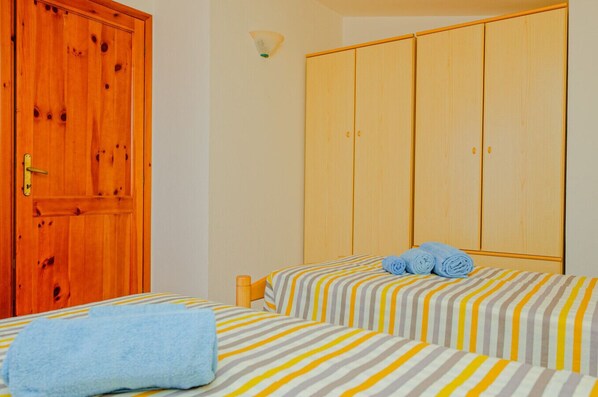 A room with two beds, a wooden wardrobe, and a wall-mounted light fixture.