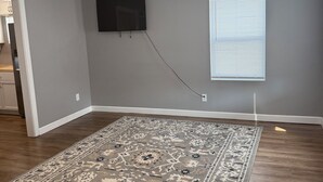 A room with a large rug, a flat-screen TV mounted on the wall, and a window with blinds. - 3-bedroom house in fabulous St. Louis with AC (St. Louis)