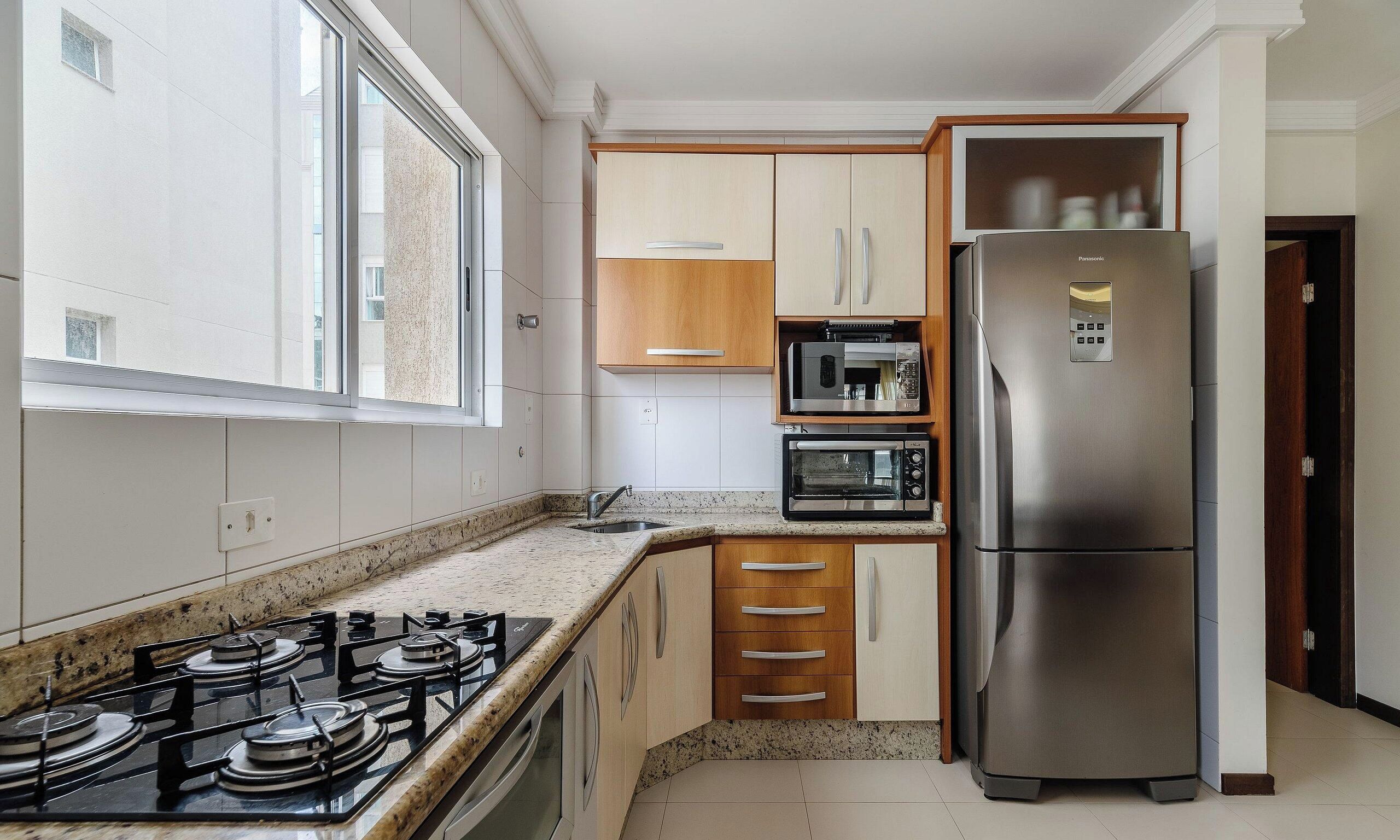 A compact kitchen with a gas stove, a built-in oven, a microwave, and a stainless steel refrigerator.