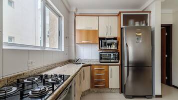 A compact kitchen with a gas stove, a built-in oven, a microwave, and a stainless steel refrigerator.
