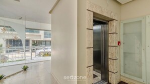 A modern building with a glass elevator, a balcony with plants, and a view of the street. - Seaview apt w/ BBQ 50m From Beach Att0602 (Itapema)
