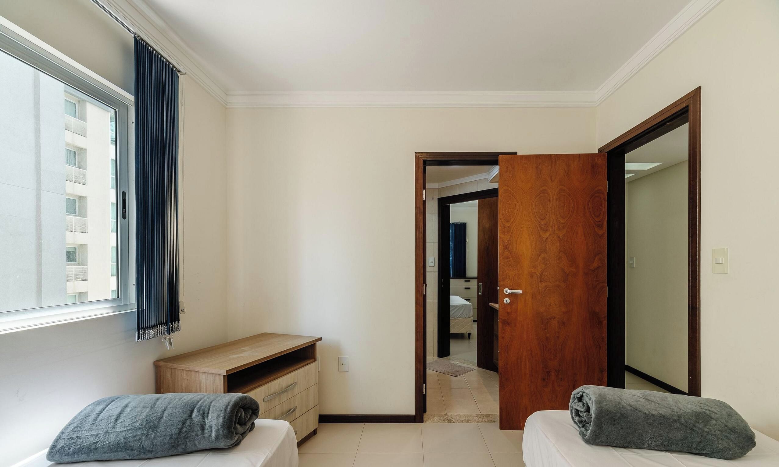 Quarto com cama, escrivaninha, guarda-roupa e janela com cortinas.