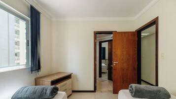 Quarto com cama, escrivaninha, guarda-roupa e janela com cortinas.