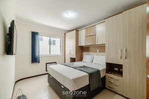 Een slaapkamer met een bed, een kledingkast, een televisie en een raam met gordijnen.
