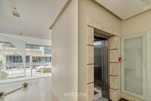A modern building with a glass elevator, a balcony with plants, and a view of the street. - Seaview apt w/ BBQ 50m From Beach Att0602 (Itapema)