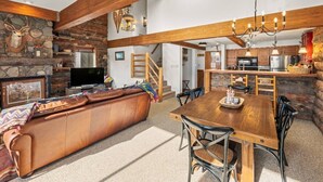 A cozy living room with a stone fireplace, a leather sofa, and a wooden dining table with chairs.