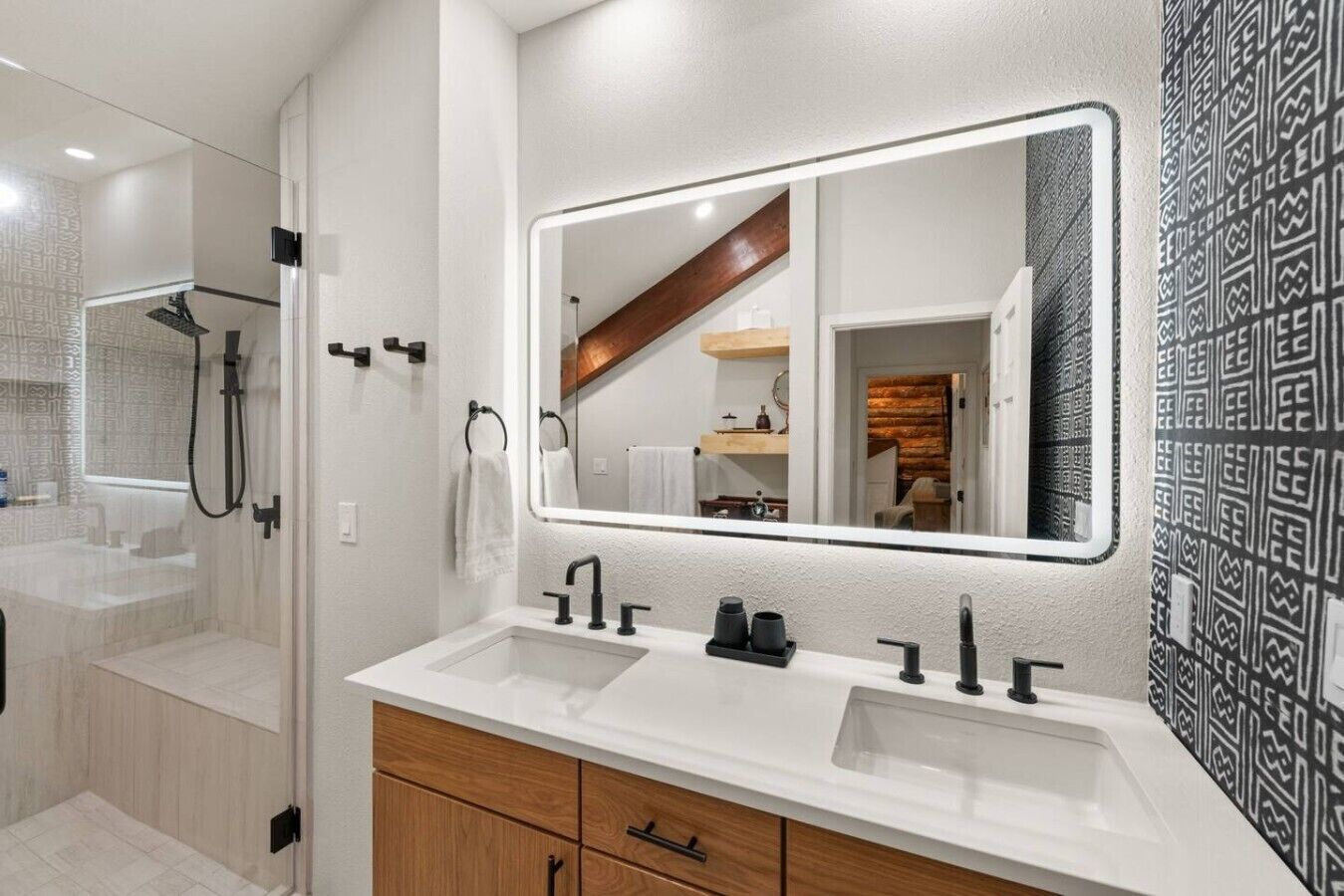 Un bagno moderno con un ampio specchio, due lavabi e mobili contenitori in legno.