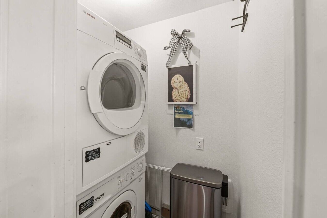 Une buanderie équipée d’un lave-linge à chargement frontal, d’un sèche-linge et d’une poubelle.