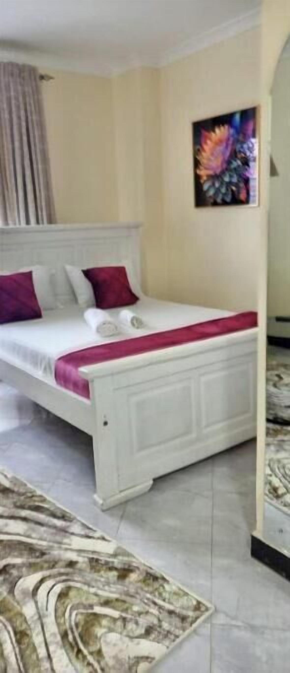 A bedroom with a bed, pillows, a painting, and a patterned rug.