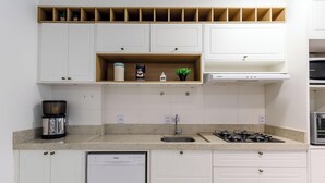 Eine moderne Küche mit weißen Schränken, einer Arbeitsplatte aus Granit, einer Kaffeemaschine, einem Gasherd und einem Geschirrspüler.