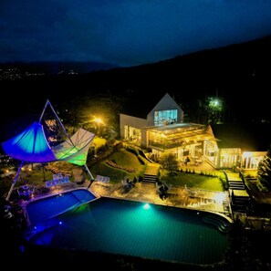 A modern house with a swimming pool, outdoor seating, and a large umbrella structure.