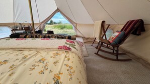 Ein Zelt mit Bett, einem Schaukelstuhl und Blick ins Freie.