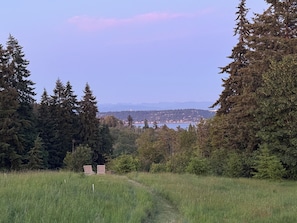 Un champ verdoyant avec deux chaises en bois, de nombreux arbres à feuilles persistantes et une vue lointaine d’une ville de l’autre côté d’une étendue d’eau.